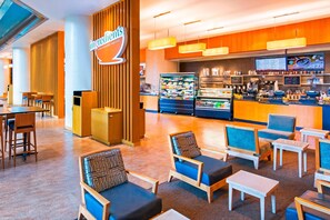 A modern cafe with wooden furniture, a counter with a menu display, and a refrigerated display case. - The Westin Cincinnati (Cincinnati)
