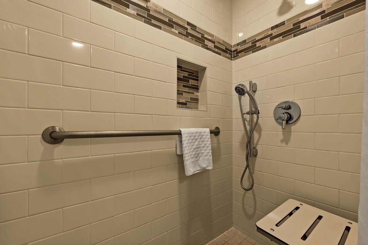 Un espacio de ducha con azulejos color beige, un perchero, un cabezal de ducha manual y una llave de control.