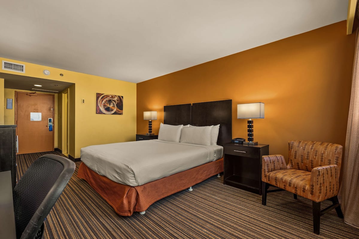 Une chambre d’hôtel avec un lit, deux tables de chevet, une chaise et un sol recouvert de moquette.