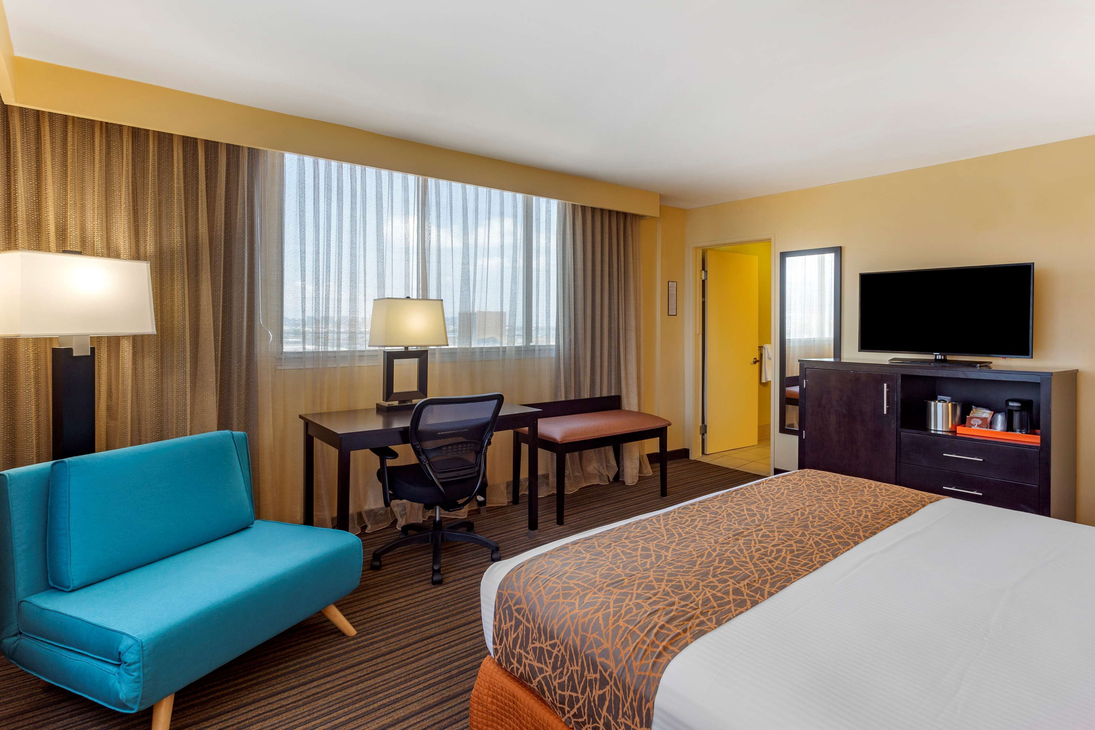 Une chambre d’hôtel équipée d’un lit, d’un bureau, d’une chaise, d’un canapé, d’une télévision et d’une fenêtre avec des rideaux.