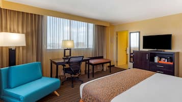 Une chambre d’hôtel équipée d’un lit, d’un bureau, d’une chaise, d’un canapé, d’une télévision et d’une fenêtre avec des rideaux.