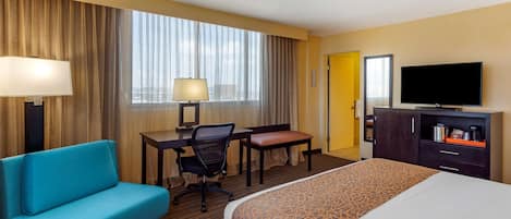Habitación de hotel con cama, escritorio, silla, sofá, televisión y ventana con cortinas.
