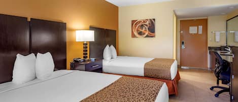 A hotel room with two beds, a desk, a chair, a lamp, and a painting on the wall.