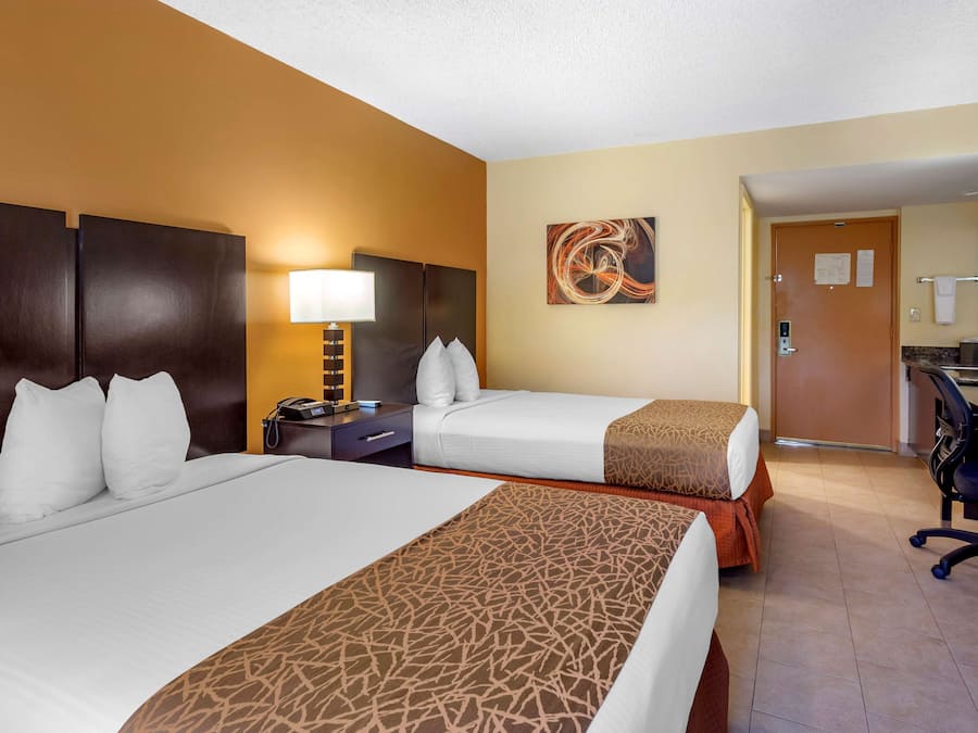 A hotel room with two beds, a desk, a chair, a lamp, and a painting on the wall.