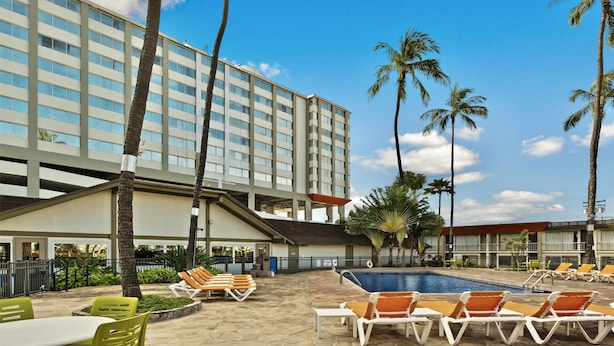 A hotel with a swimming pool, lounge chairs, palm trees, and a multi-story building.