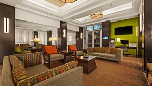 A modern hotel lobby with sofas, armchairs, a coffee table, and a flat-screen TV.