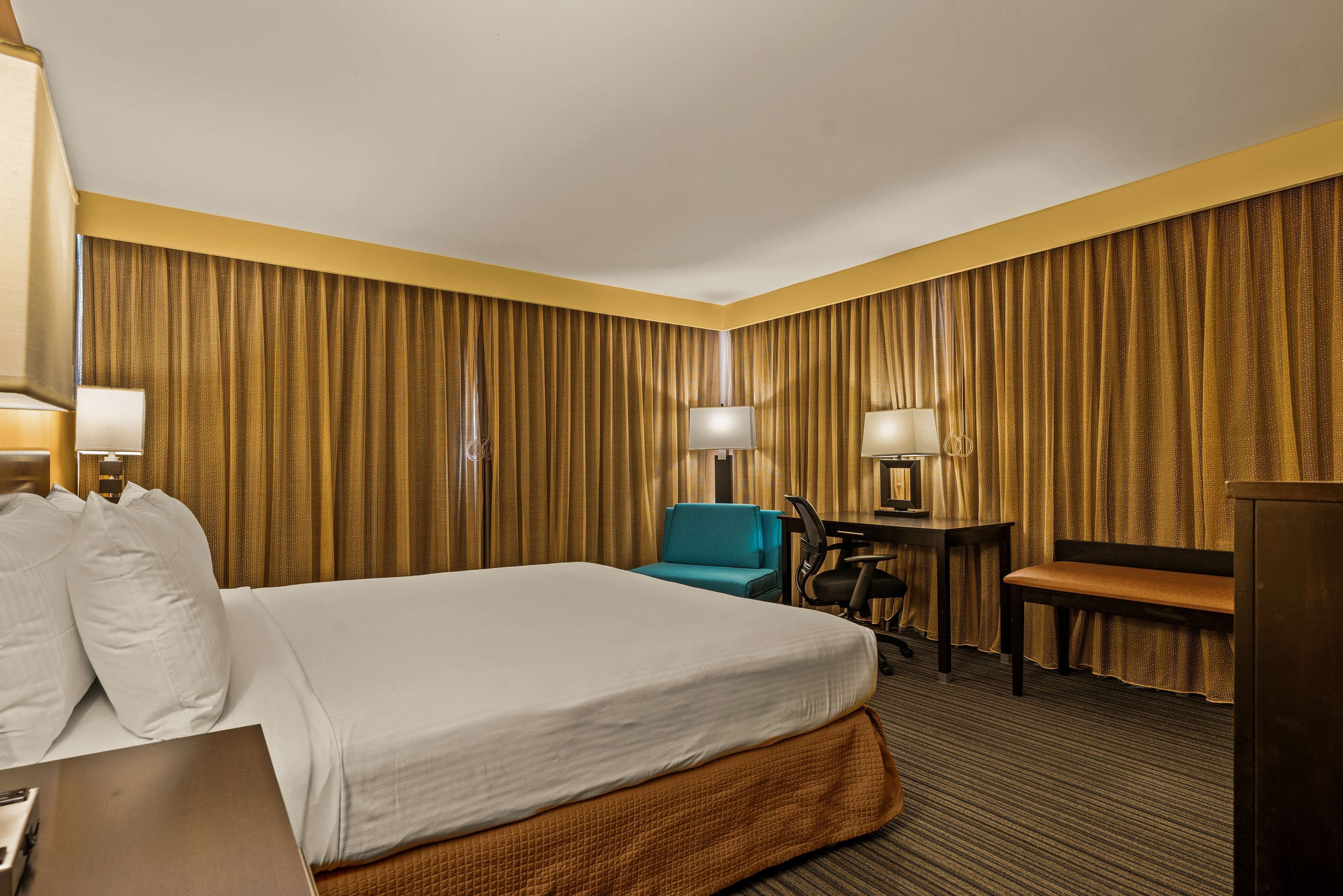 A hotel room with a large bed, a desk, a chair, and a desk lamp.