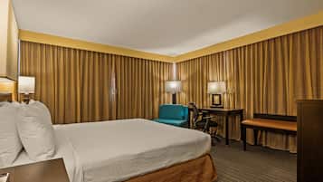 A hotel room with a large bed, a desk, a chair, and a desk lamp.