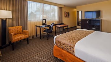 A hotel room with a large bed, a desk with a computer, a chair, a TV, and a lamp.