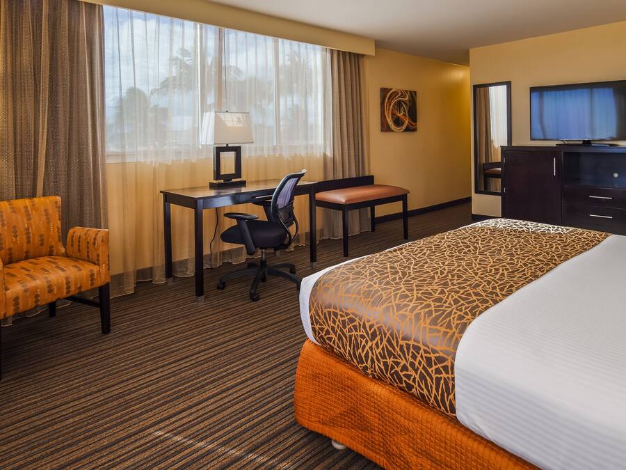 A hotel room with a large bed, a desk with a computer, a chair, a TV, and a lamp.