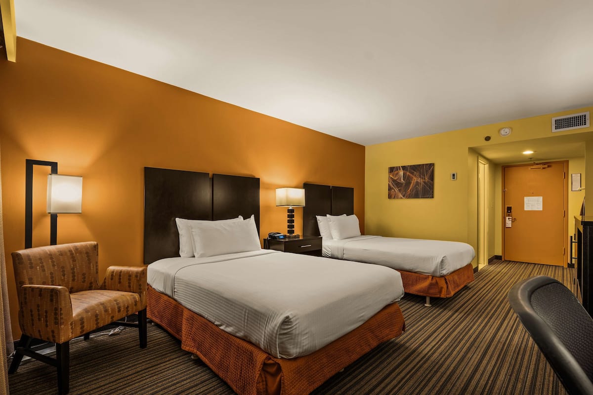 Une chambre d’hôtel avec deux lits, une chaise, un bureau et une lampe.