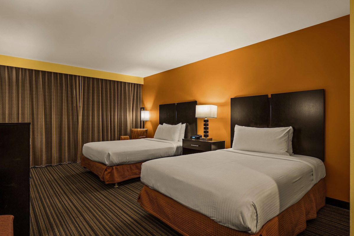 Una habitación de hotel con dos camas, televisión, escritorio y lámpara.