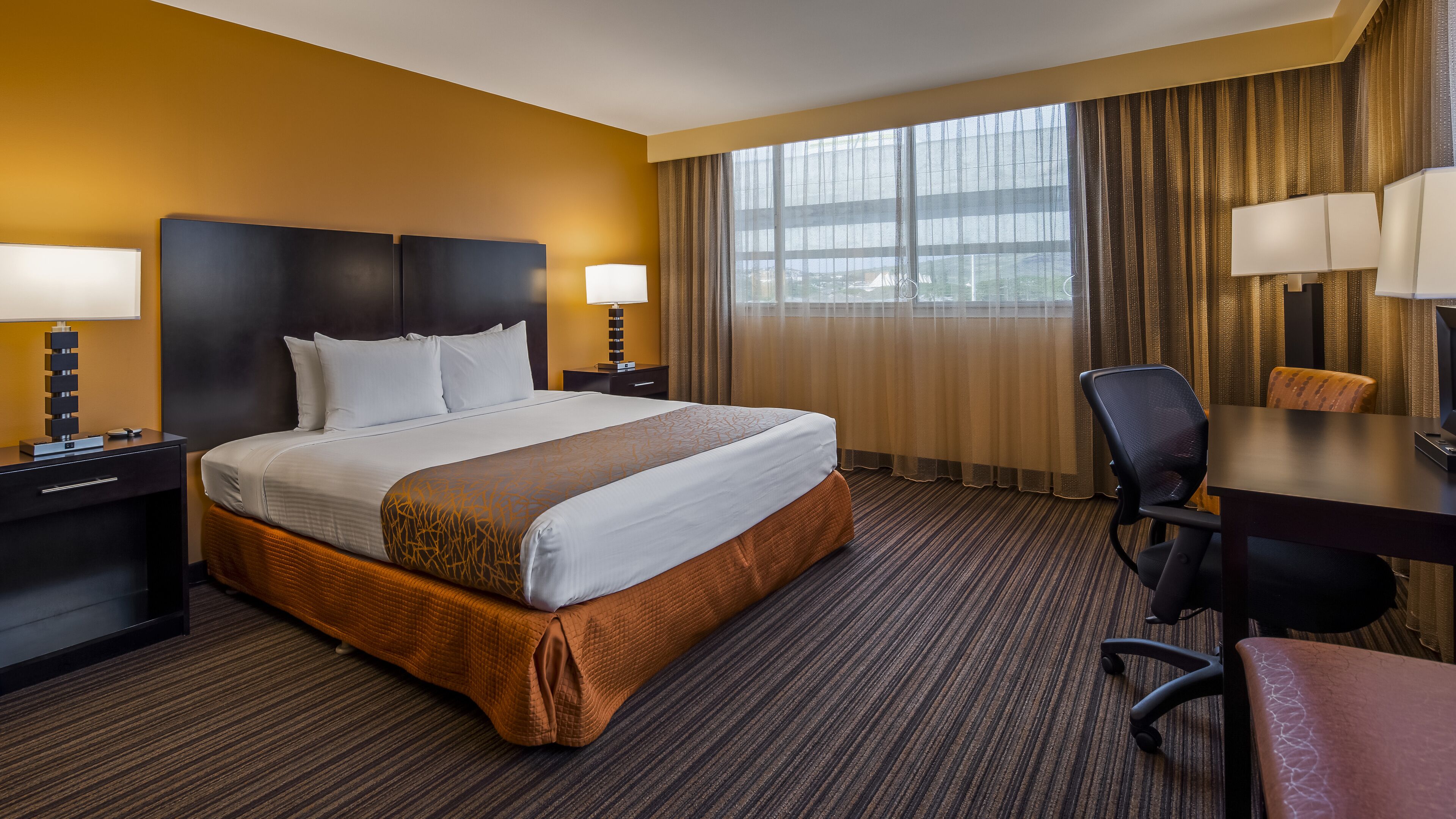 A hotel room with a large bed, two bedside tables with lamps, a desk, and a chair.