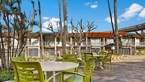 A hotel patio with outdoor seating, palm trees, and a building with balconies.