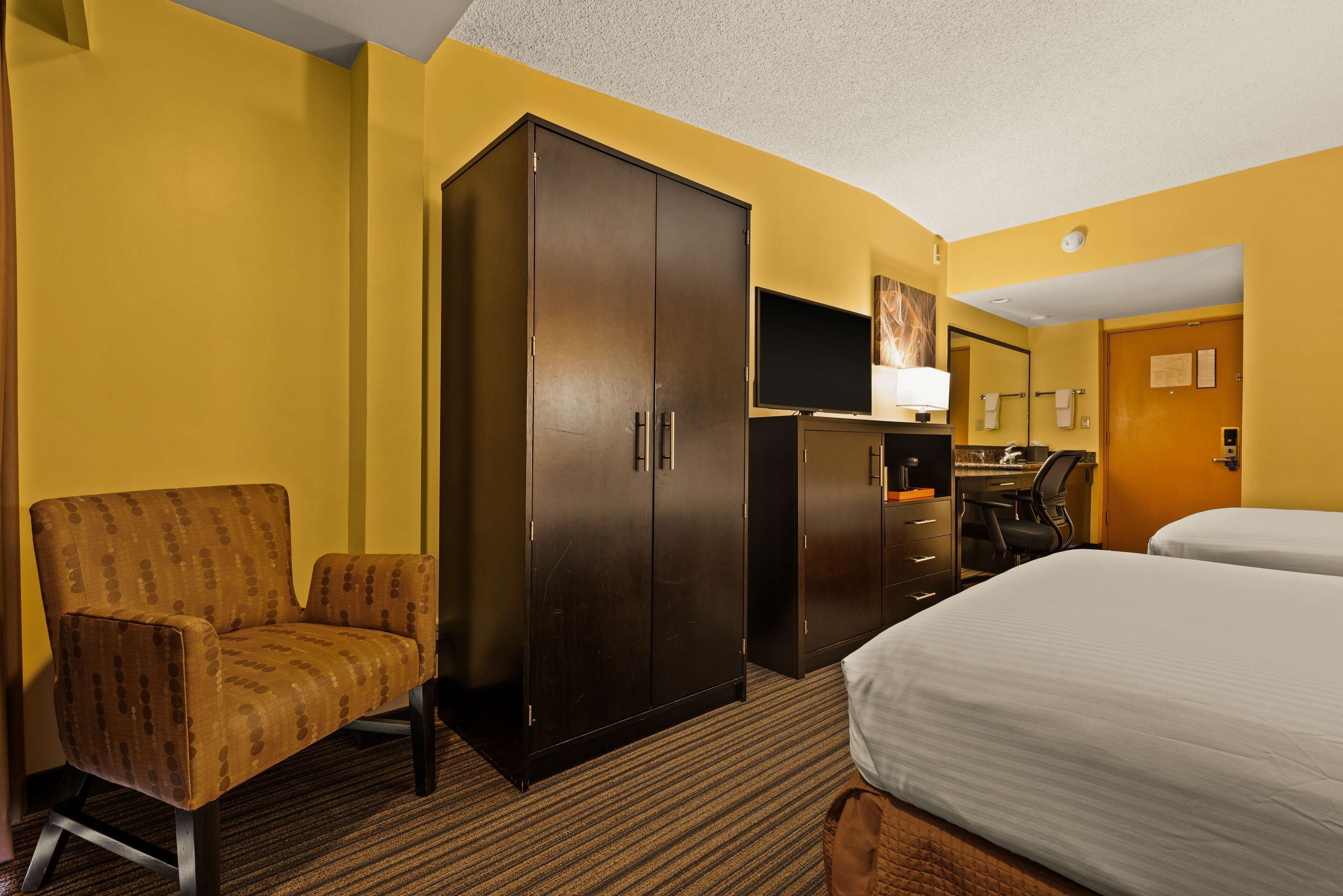 A hotel room with a bed, a chair, a desk, a wardrobe, and a television.