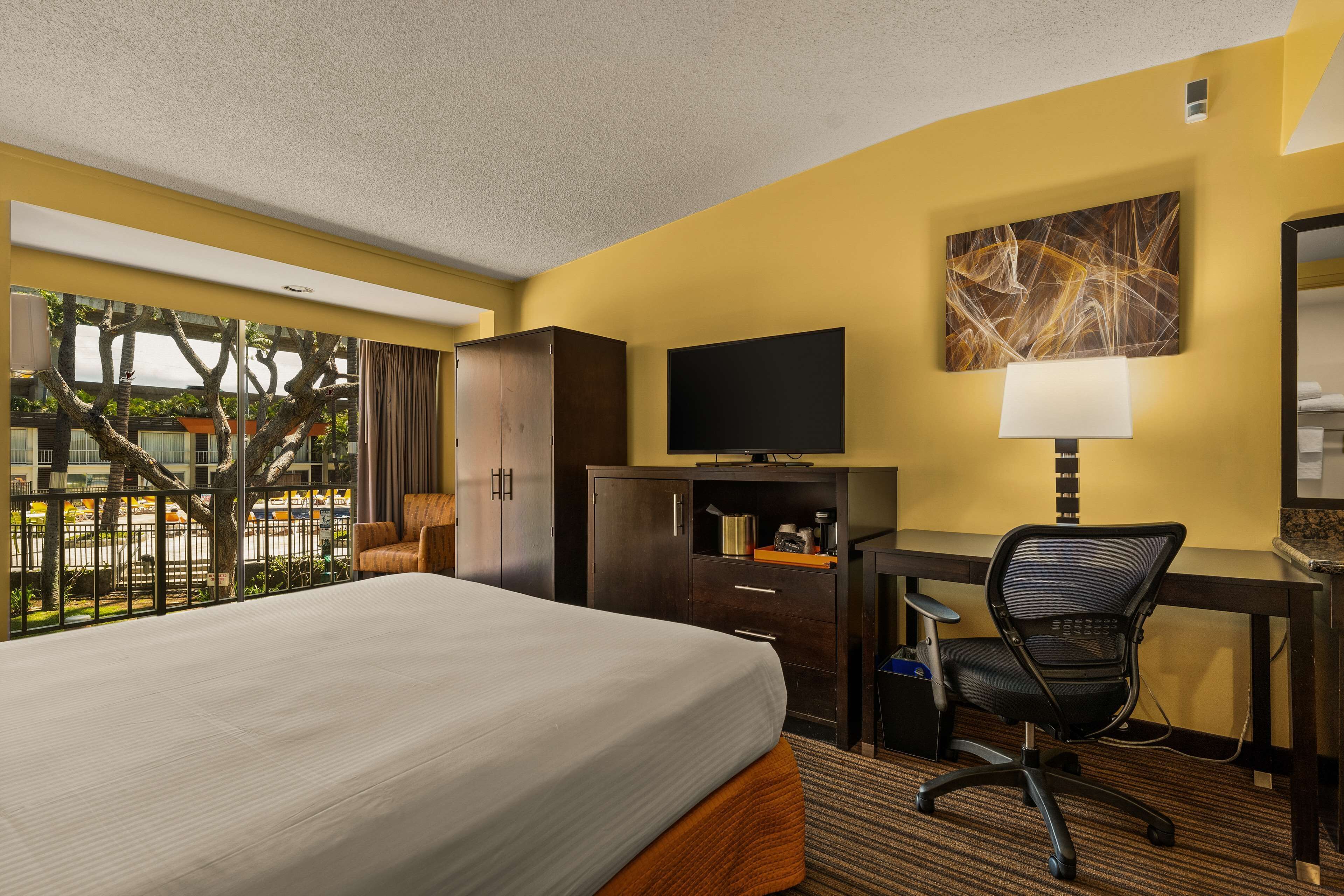 A hotel room with a bed, desk, chair, television, and artwork on the wall.