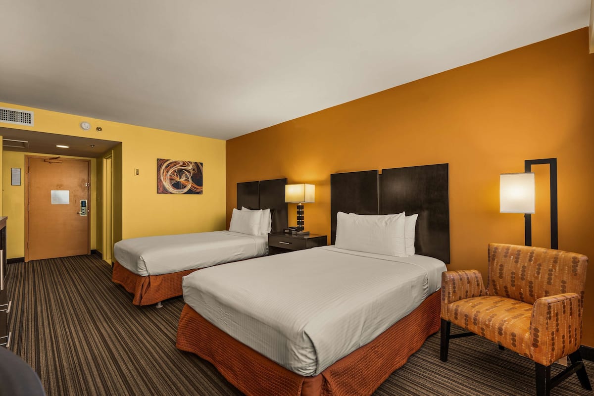 Une chambre d’hôtel avec deux lits, une chaise, une table de chevet et un tableau au mur.
