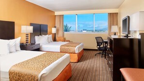 A hotel room with two beds, a desk, a chair, a television, and a view of the city.