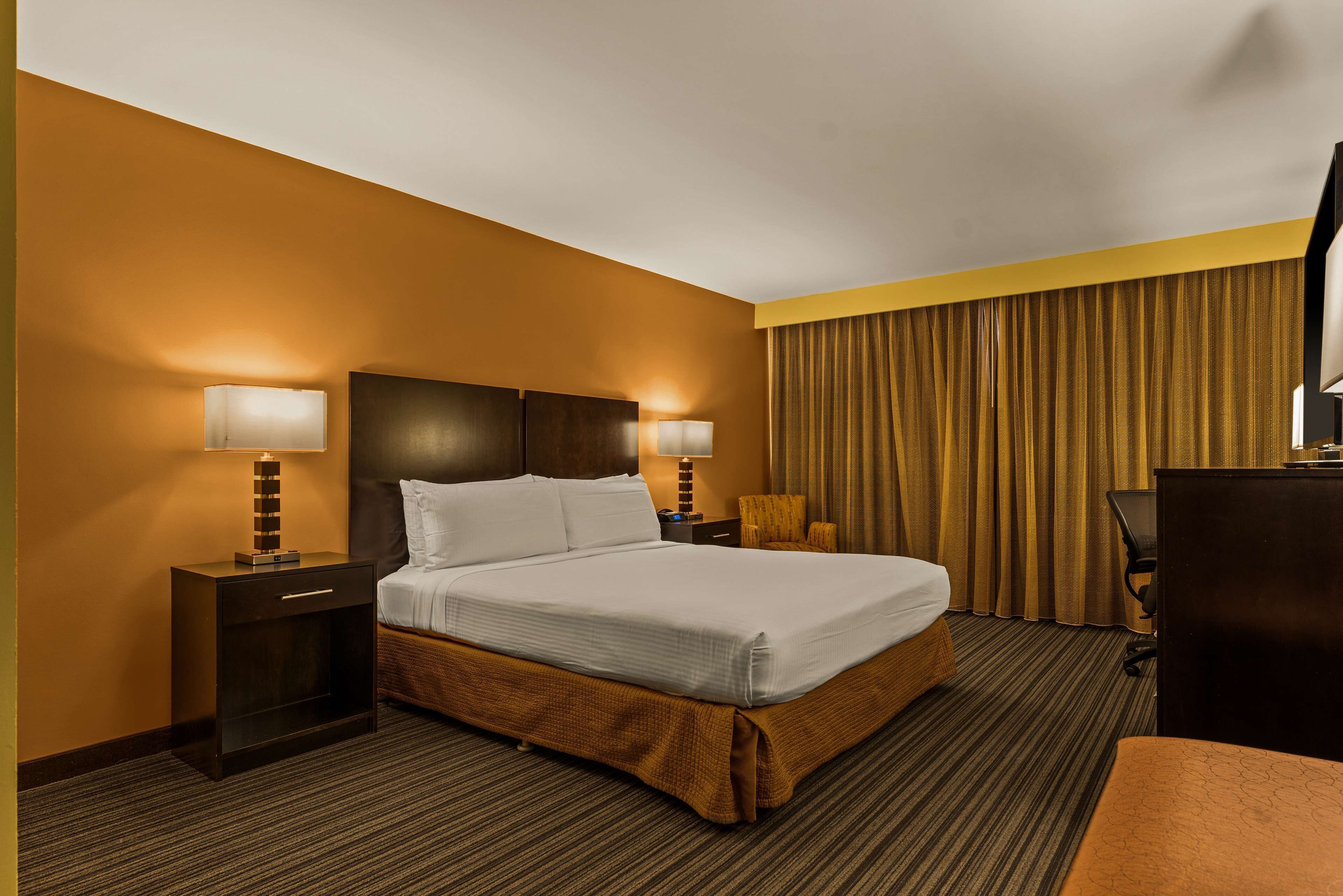 A hotel room with a large bed, two bedside tables with lamps, a desk, and a chair.