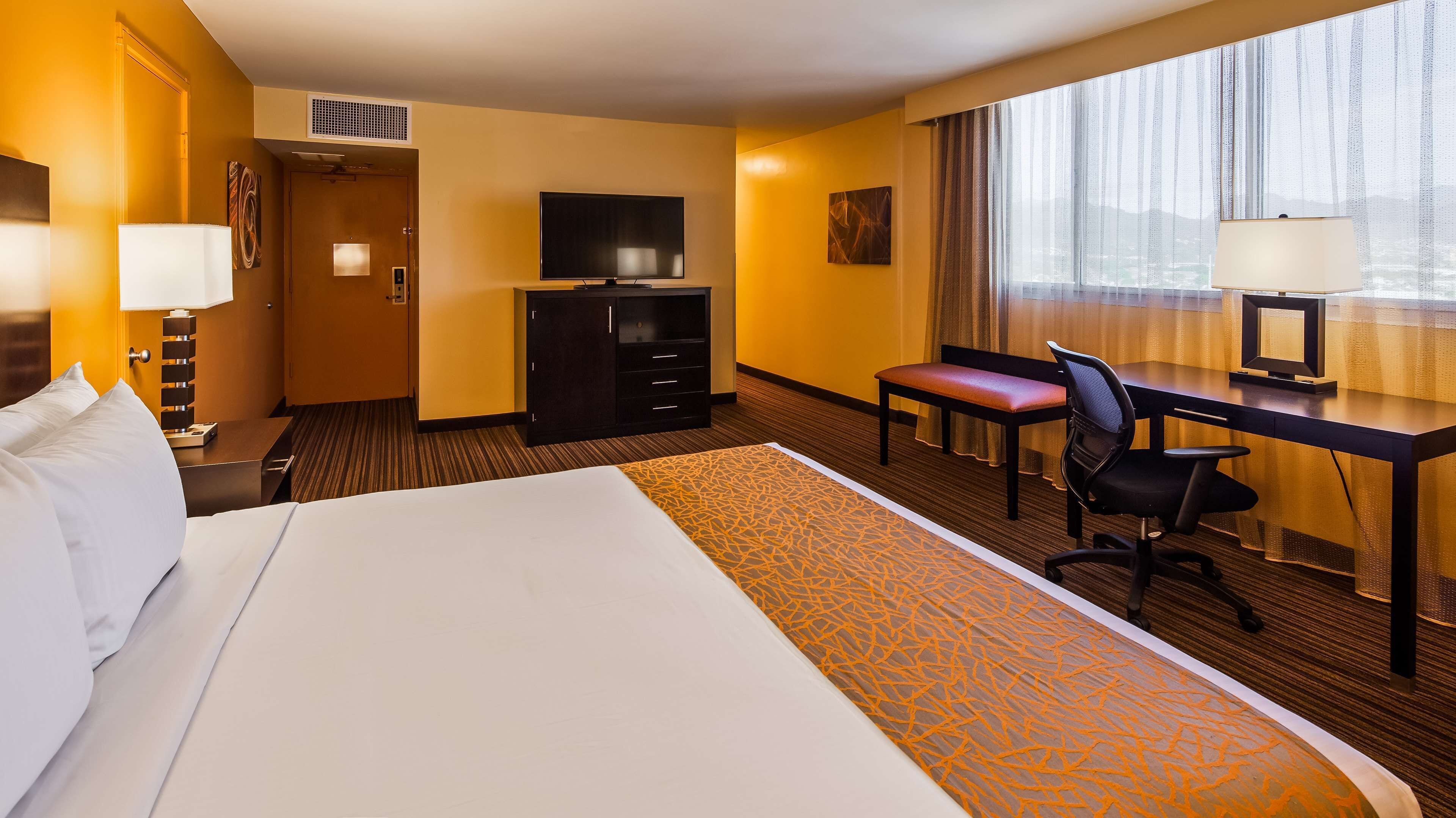 Una habitación de hotel con una cama grande, un escritorio con silla, televisión y una ventana con cortinas.