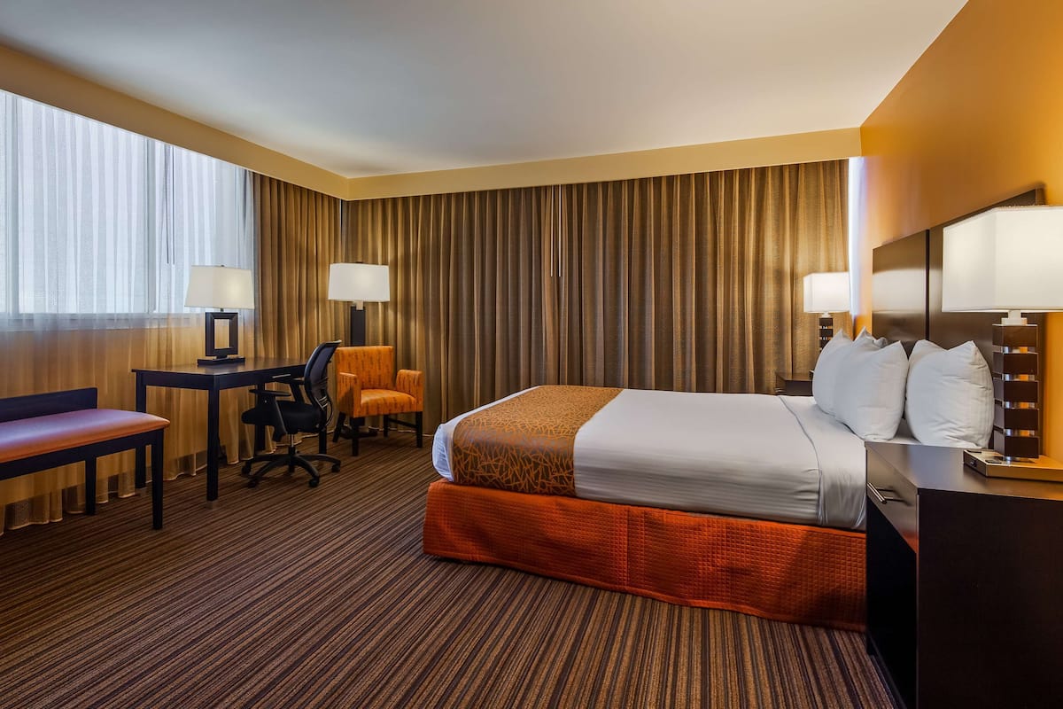 Une chambre d’hôtel avec un grand lit, un bureau, une chaise, un banc et une lampe.
