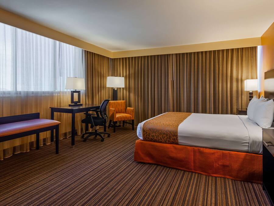 A hotel room with a large bed, a desk, a chair, a bench, and a lamp.