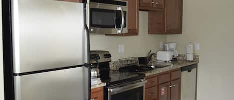 A kitchen with a stainless steel refrigerator, a microwave, an oven, wooden cabinets, and a granite countertop.