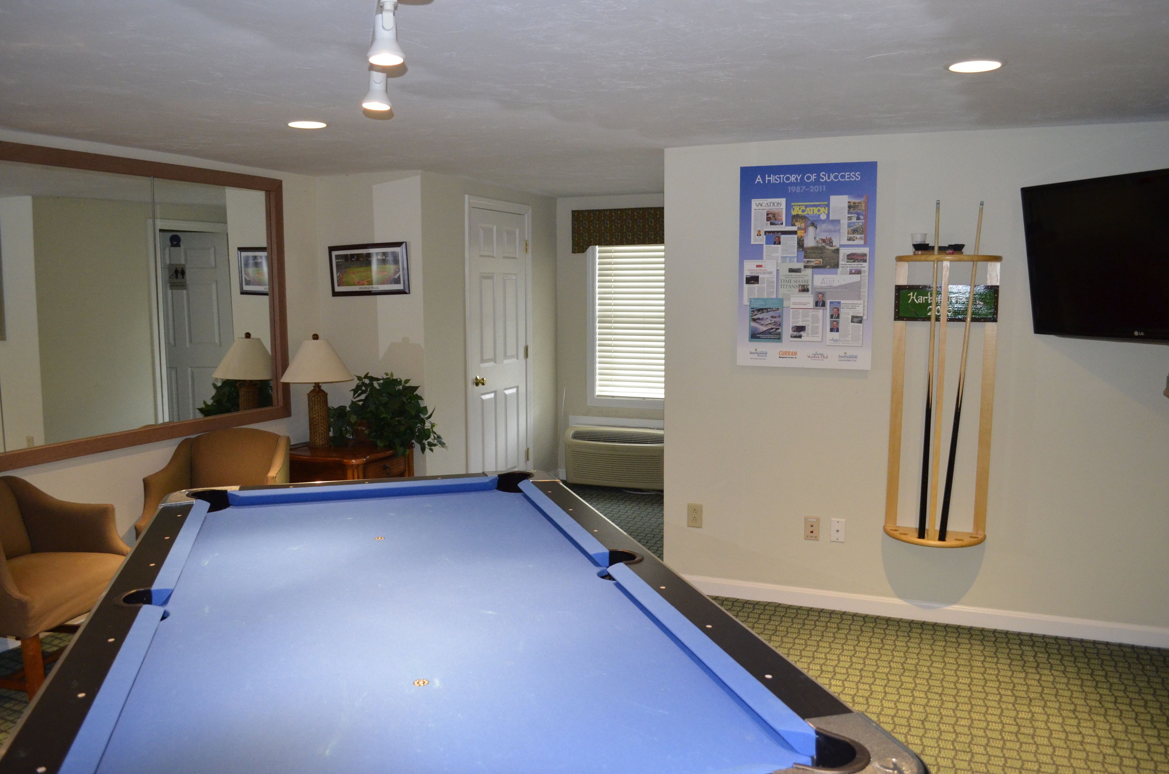 A pool table in a room with a poster on the wall, a television, and a door.