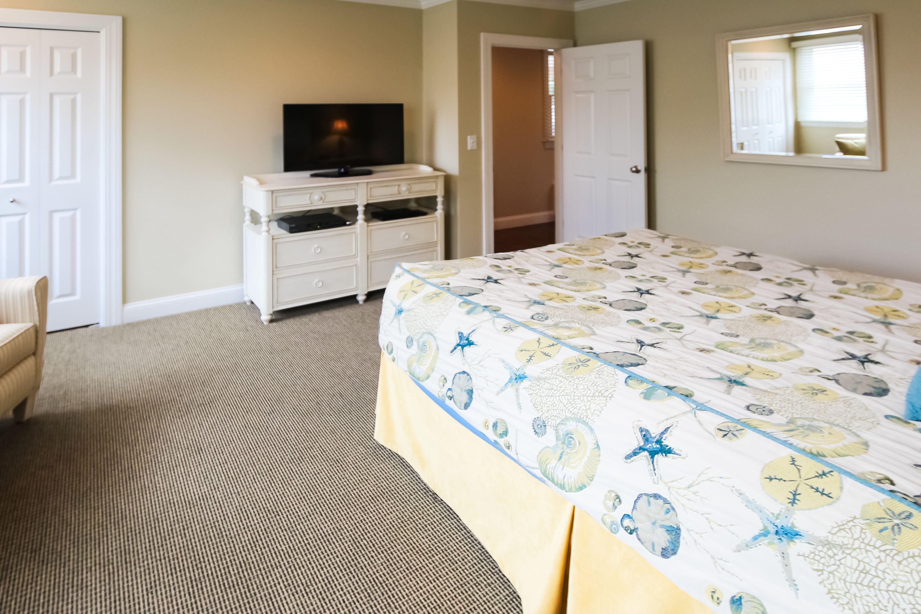 A bedroom with a bed, a dresser, a television, and a door leading to another room.