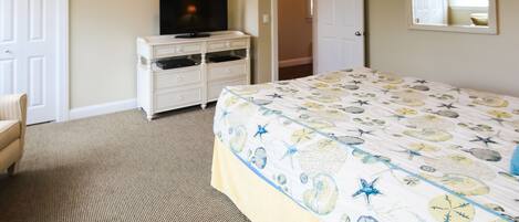 A bedroom with a bed, a dresser, a television, and a door leading to another room.