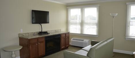 A living room with a sofa, a television, a small table, and a window with blinds.