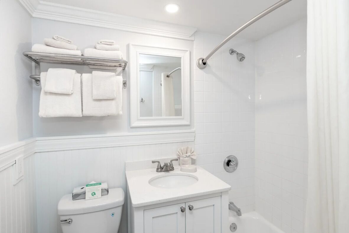 Une salle de bain avec des toilettes, un lavabo et une douche. Des serviettes sont posées sur une étagère au-dessus des toilettes.