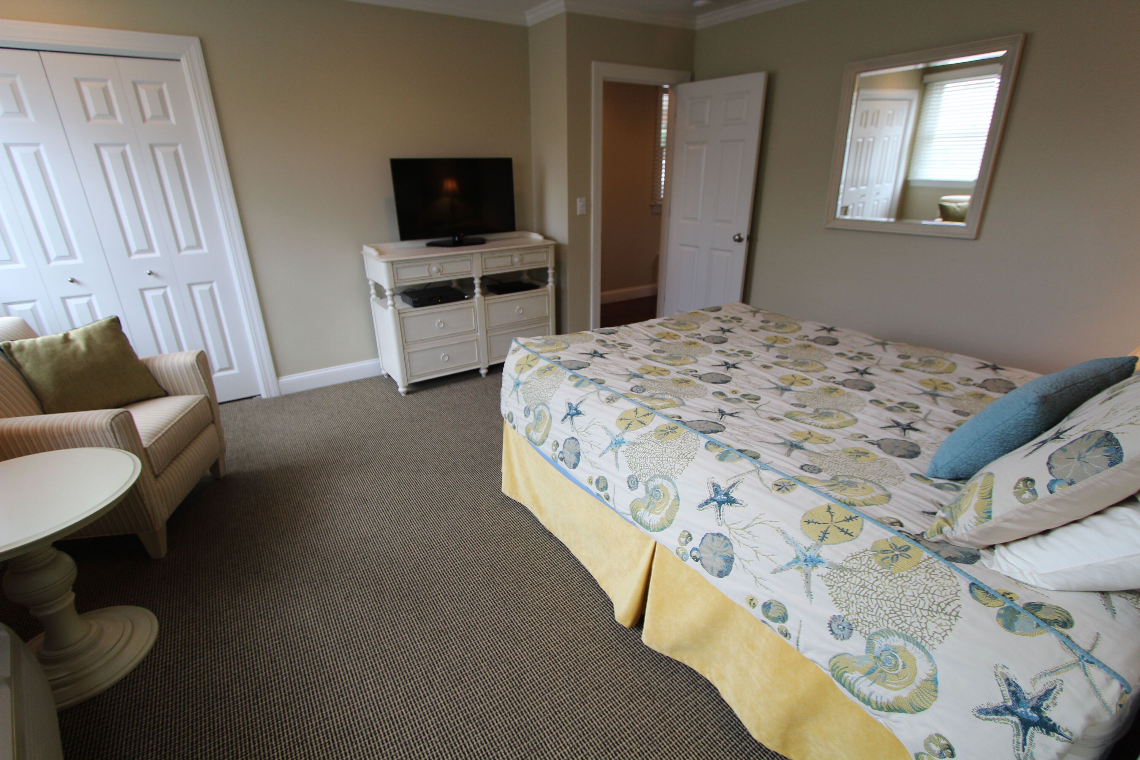 A hotel room with a bed, a television on a dresser, a chair, and a small table.