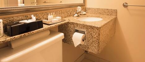 A bathroom with a granite countertop, a sink, a toilet, and a mirror.