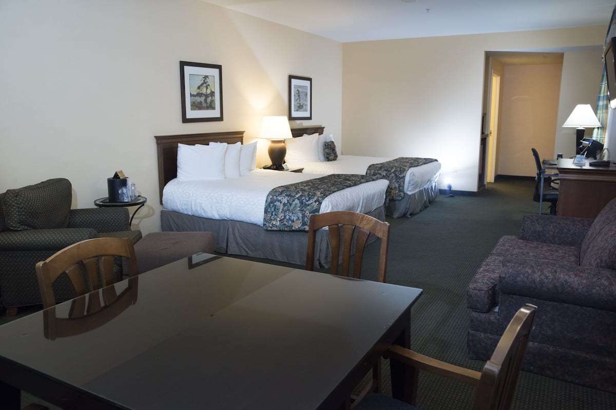 A hotel room with two beds, a dining table, and a seating area.