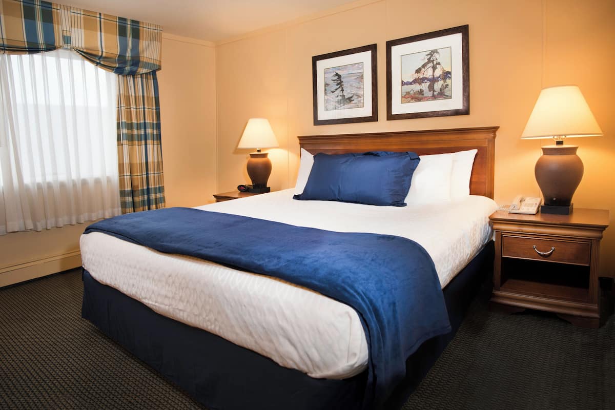 A hotel room with a large bed, two bedside lamps, a nightstand, and a window with curtains.