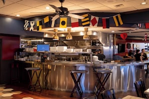 Un interior de restaurante con una zona de bar, electrodomésticos de acero inoxidable y un ventilador de techo.