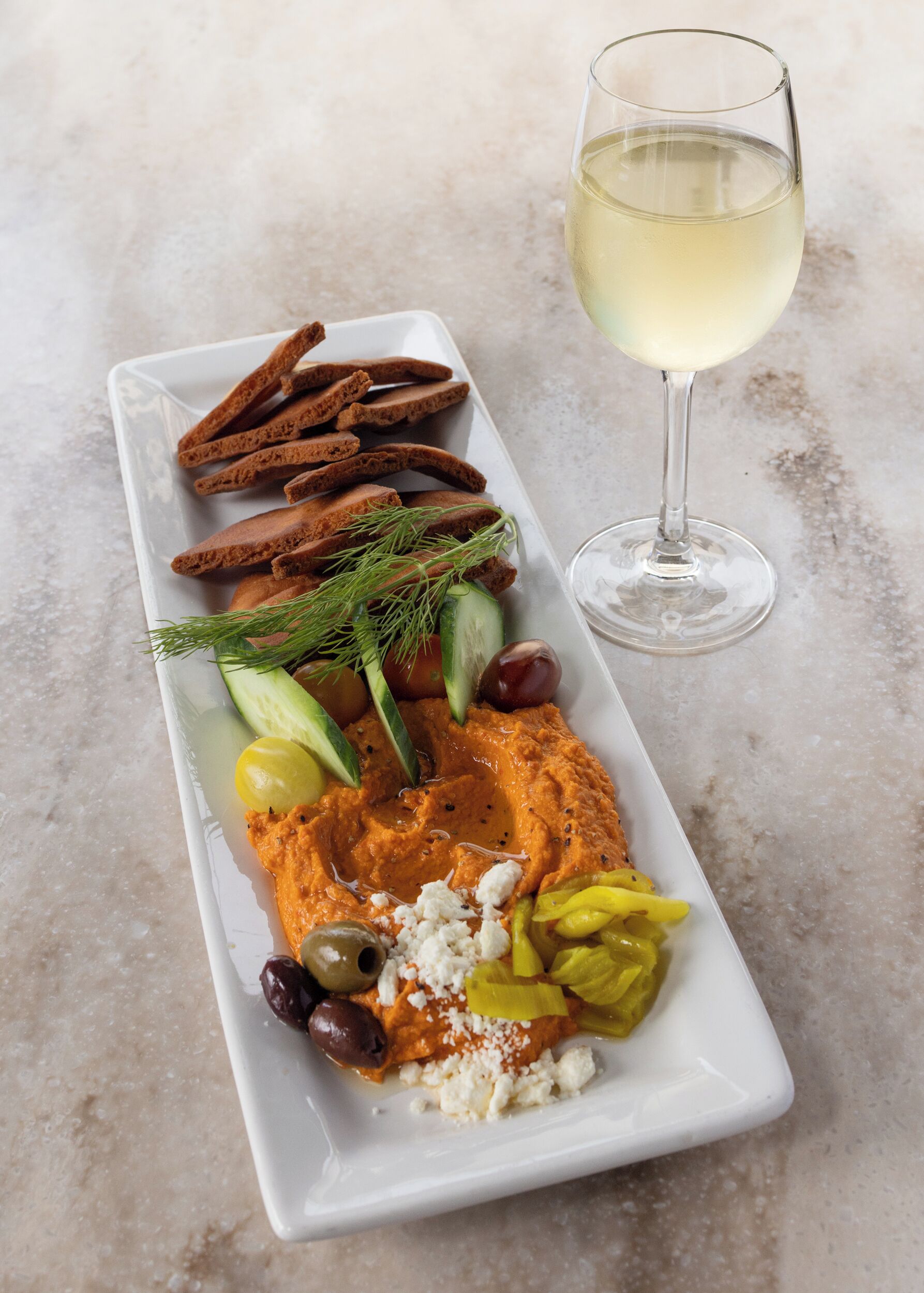 A rectangular white plate with various food items and a glass of white wine.