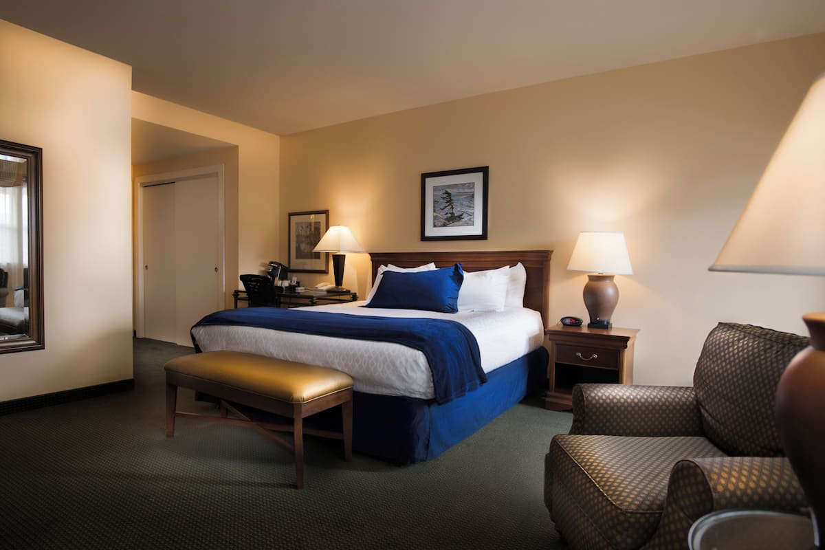 A hotel room with a bed, bedside tables, a bench, a chair, and a framed picture on the wall.