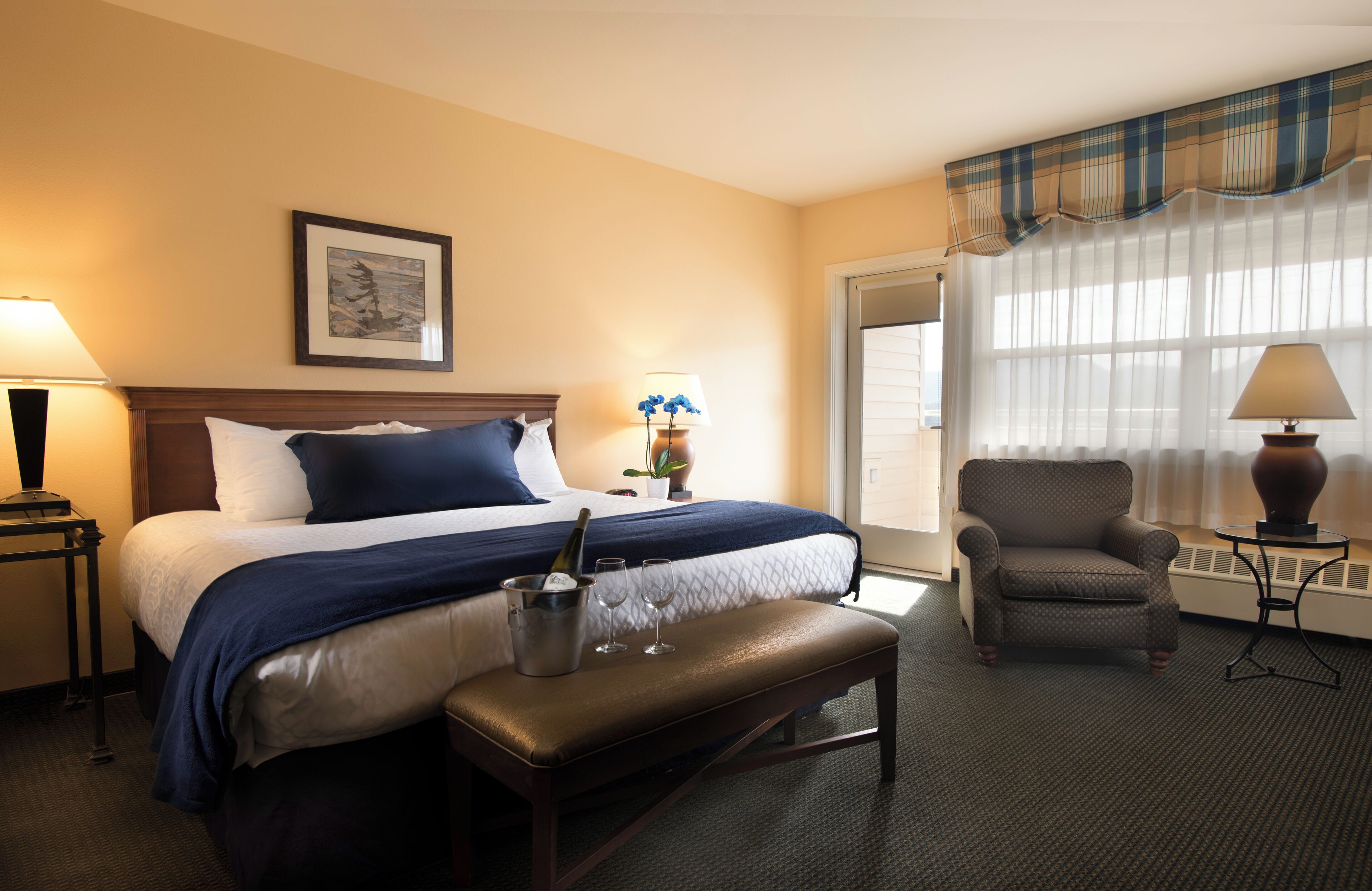 Una habitación de hotel con cama, una silla, una mesa y un ventanal con cortinas.