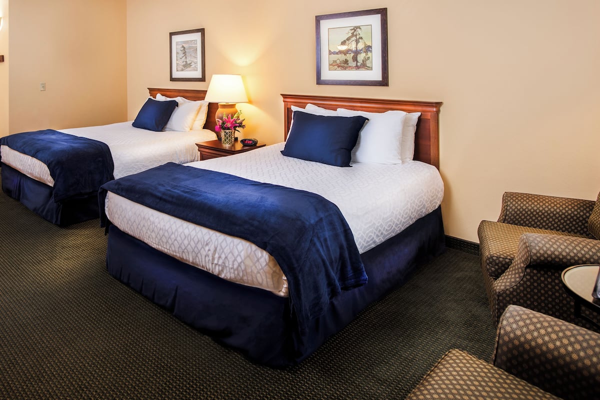 A hotel room with two beds, a nightstand with a lamp, a chair, and two framed pictures on the wall.