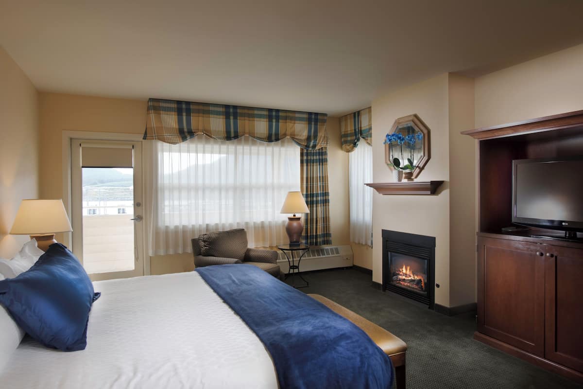A hotel room with a bed, a television, a fireplace, and a view of the outside.