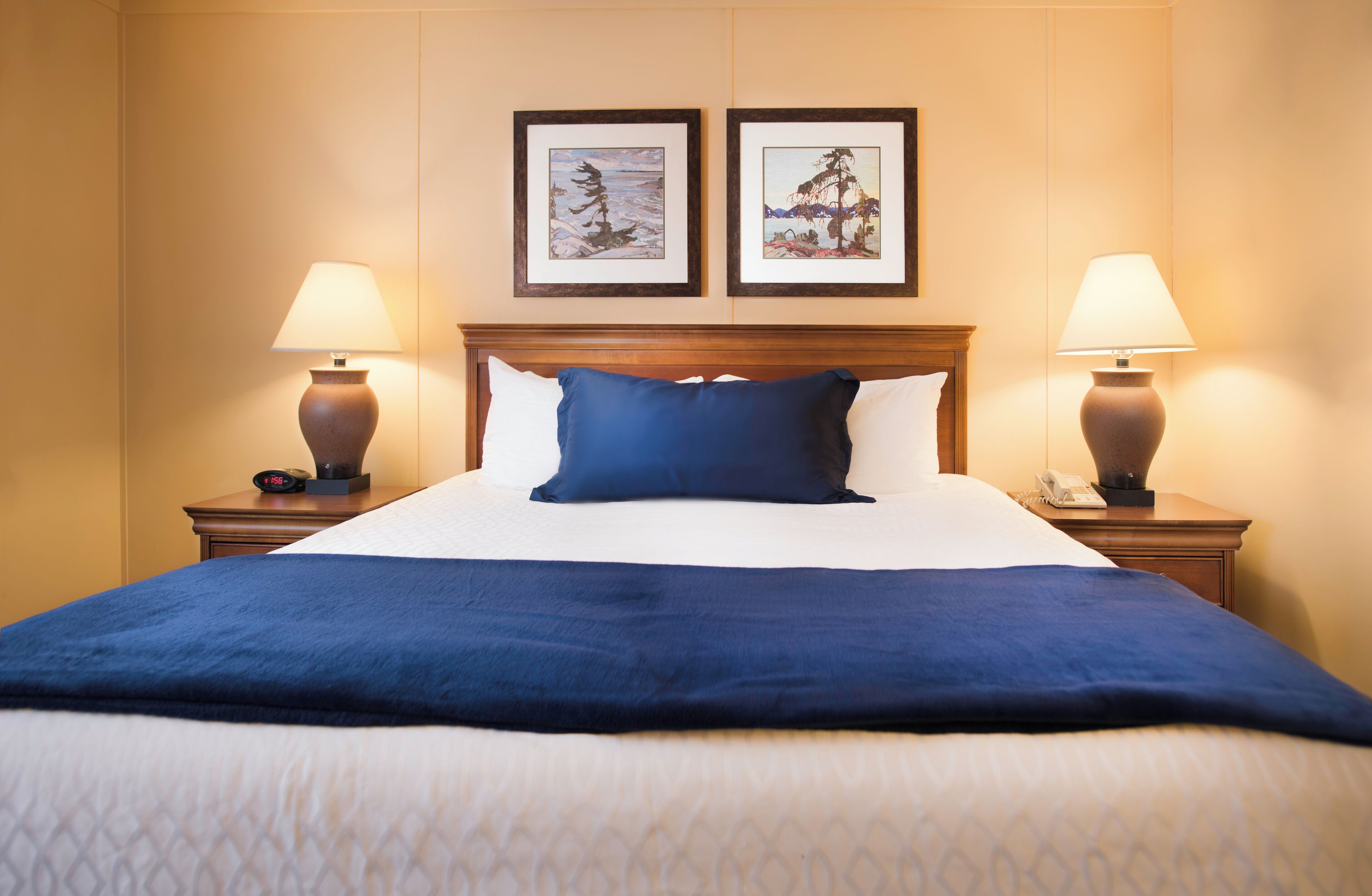 A hotel room with a large bed, two framed pictures on the wall, and two bedside lamps.