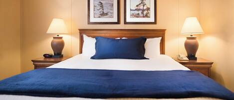 A hotel room with a large bed, two framed pictures on the wall, and two bedside lamps.