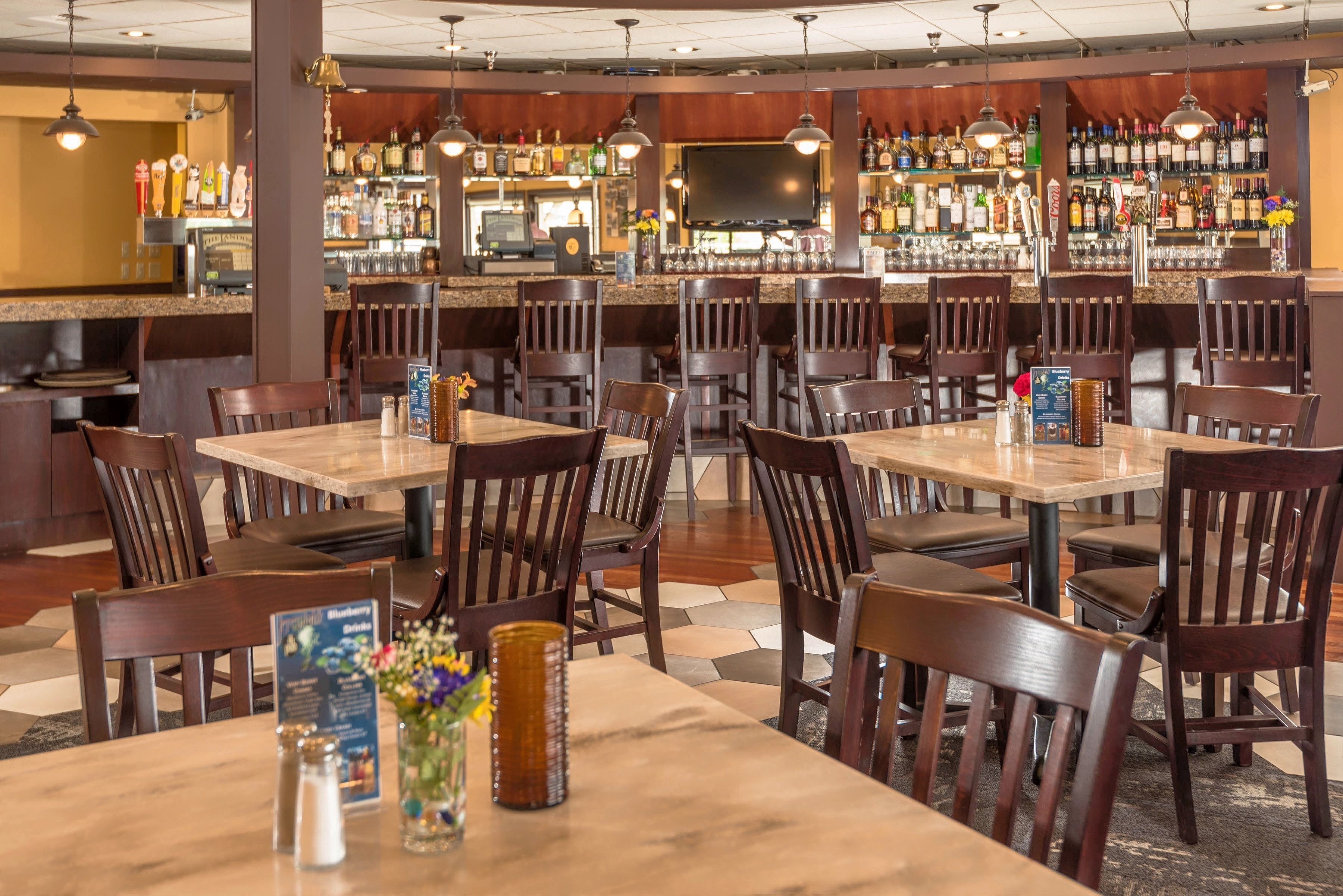 A restaurant with multiple tables and chairs, a bar area with a variety of bottles, and a television screen.