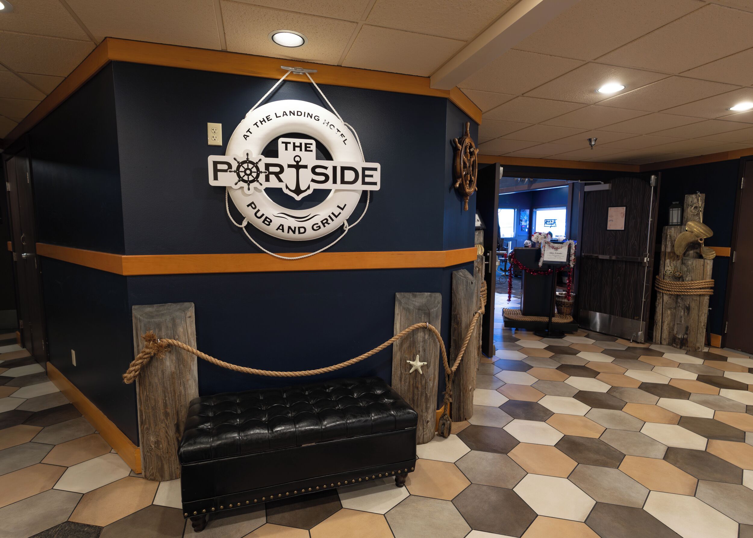 A pub and grill named 'The Portside' with a nautical theme, including a sign with a ship's wheel and anchor, a black leather bench, and a checkered floor.