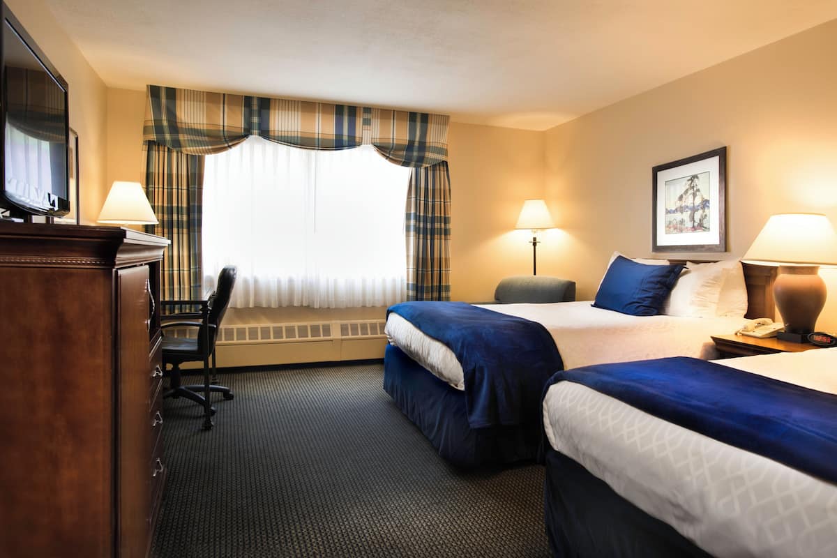 A hotel room with two beds, a desk with a chair, a TV, and a window with curtains.