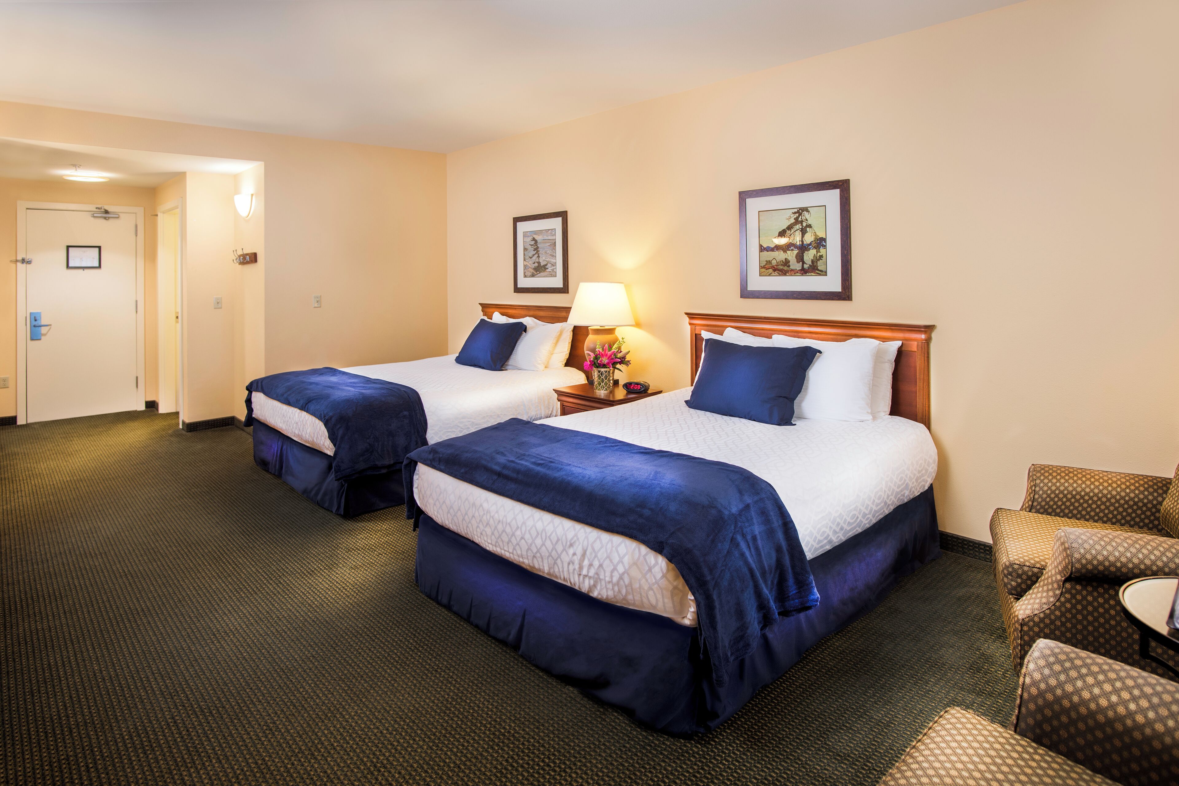 A hotel room with two beds, a sitting area, and a door leading to a hallway.