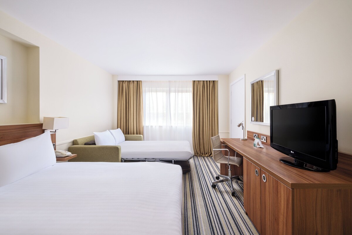A hotel room with two beds, a desk with a television, and a window with curtains.
