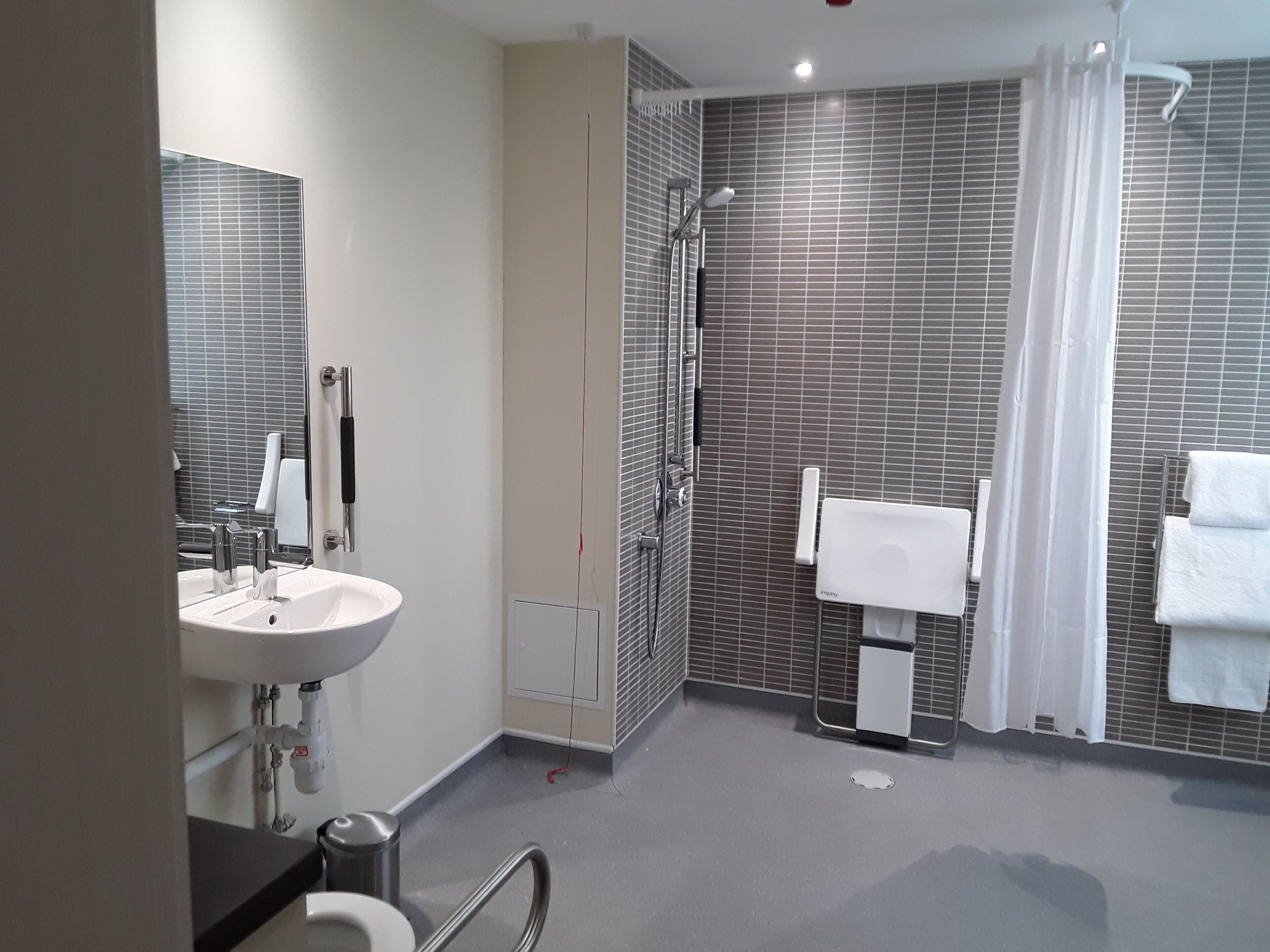 A modern bathroom with a sink, mirror, shower, and towel rack.